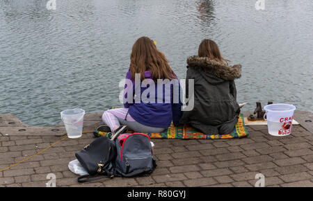 Lymington, Angleterre - 25 octobre 2018 : la pêche de crabe par deux jeunes filles dans le port de Lymington avec deux petits seaux et certains sacs. Banque D'Images