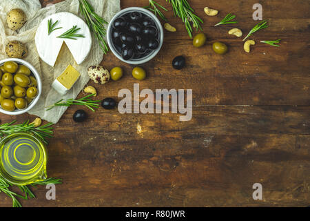 Ensemble de camembert fromage, olives noires et vertes, des oeufs de cailles sur des plaques, l'huile d'olive et le romarin, noix de cajou, sur la vieille table en bois sombre arrière-plan. Top v Banque D'Images