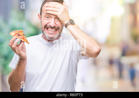 L'âge moyen des cadres supérieurs des man eating pizza slice sur fond isolé a souligné avec la main sur la tête, choqué par la honte et la surprise face, en colère et fr Banque D'Images
