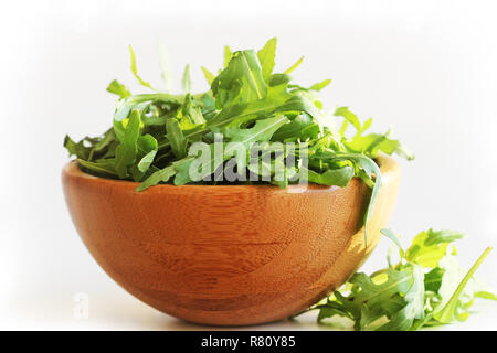 Feuilles de roquette fraîche dans bol en bois, rucola sur fond blanc Banque D'Images