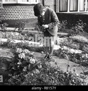 Années 1950, la photographie du film, historique, un écolier à l'extérieur d'un jardin fleuri pour prendre des photos de fleurs avec un Kodak Brownie 'réflexe' film appareil, England, UK. Une mise au point fixe, l'appareil photo à double objectif, c'était une simple caméra mais populaire de l'époque, en particulier à ceux qui se lancent dans la photographie. Banque D'Images