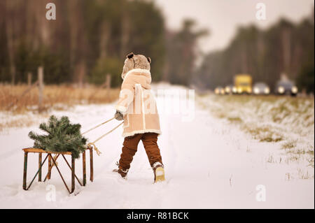 Un enfant décorer un arbre de Noël à l'extérieur. Le garçon se bloque et bulles rouge mange gingerbreads. Il est habillé d'un manteau en peau de mouton vert, dans l'arrière-plan Banque D'Images