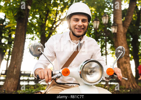 Jeune homme d'excités en équitation casque sur une moto à l'extérieur dans le parc de la ville Banque D'Images