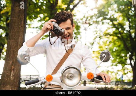 Happy young businessman riding sur une moto à l'extérieur, prendre des photos avec un appareil photo Banque D'Images