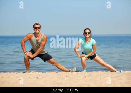 Smiling couple stretching jambes on beach Banque D'Images