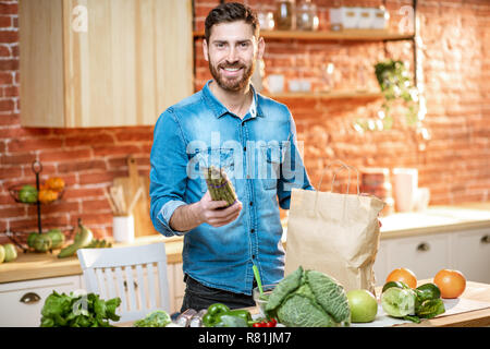 Bel homme en chemise bleue le déballage des aliments sains à partir de votre panier sur la cuisine Banque D'Images