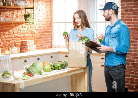 Client produits femme cheking permanent avec livraison sur le travailleur à domicile cuisine Banque D'Images