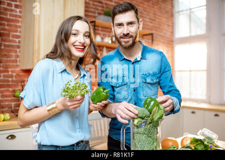 Portrait d'un jeune couple de végétariens en chemises bleues faire avec smoothie vert frais produits sur la cuisine à la maison Banque D'Images