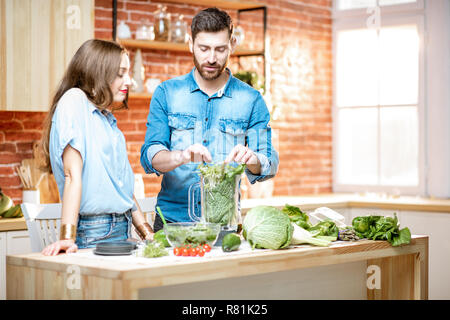 Jeune couple de végétariens en chemises bleues faire avec smoothie vert frais produits sur la cuisine à la maison Banque D'Images