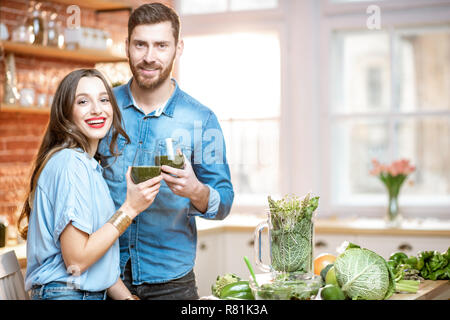 Portrait d'un jeune couple de végétariens frais potable sur smoothie la cuisine avec des aliments sains à la maison verte Banque D'Images