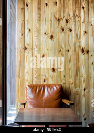 Cafe de l'intérieur avec la lumière brown vintage canapé en cuir et table basse en bois sur fond de bois vierge près de la fenêtre en verre style vertical. Banque D'Images