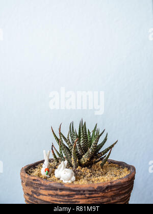 Close up cactus ou plante succulente avec de minuscules poupées lapin blanc décoration à petit semoir en terre cuite sur fond blanc avec un minimum d'espace de copie Banque D'Images