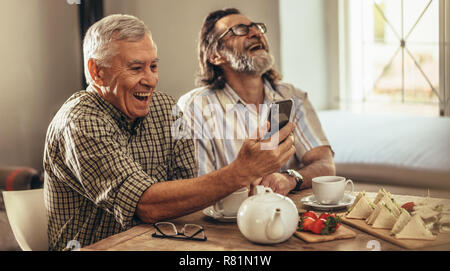 Deux heureux retraités à la recherche de photographies anciennes et de rire ensemble. Bénéficiant d'amis de sexe masculin à la maison tout en regardant leurs vieux souvenirs sur sm Banque D'Images