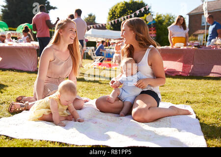 Deux mères avec leurs bébés sur tapis au jardin d'été Fete Banque D'Images