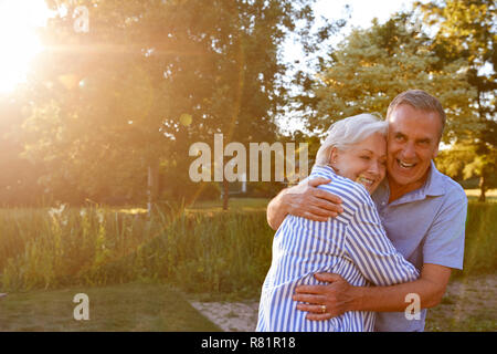Portrait de Senior Couple Hugging Outdoors in Summer Park contre Sun Torchage Banque D'Images