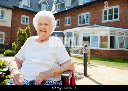 Portrait of Senior Woman Sitting hors Maison de Retraite en fauteuil roulant motorisé. Banque D'Images