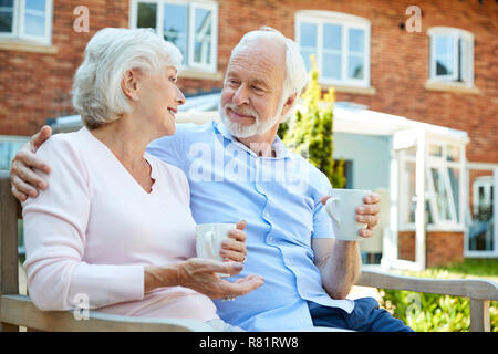 Couple de retraités assis sur un banc avec boisson chaude en résidence-services Banque D'Images
