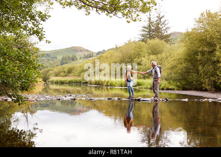 Senior Couple Crossing River alors que la randonnée au Royaume-Uni Lake District Banque D'Images