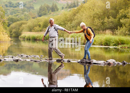 Senior Couple Crossing River alors que la randonnée au Royaume-Uni Lake District Banque D'Images