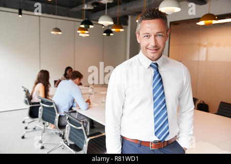 Portrait Of businessman standing dans la salle de réunion moderne avec des collègues autour de la table en arrière-plan Banque D'Images