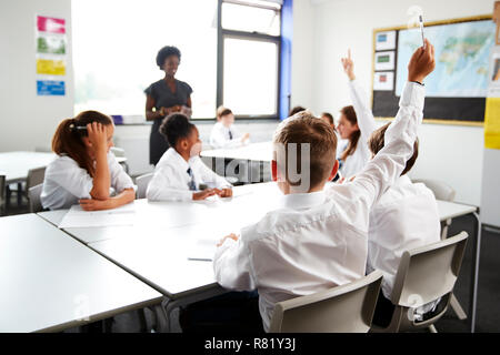 Les élèves du secondaire en uniforme élever les mains pour répondre à question posée par Teacher In Classroom Banque D'Images