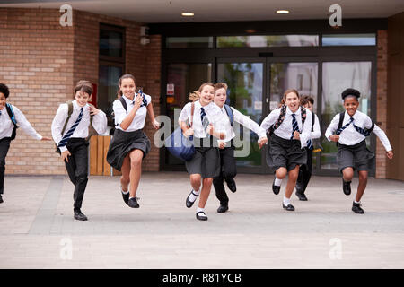 Groupe d'élèves du secondaire en uniforme à court de bâtiments scolaires vers la caméra à la fin de la classe Banque D'Images