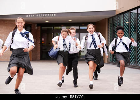 Groupe d'élèves du secondaire en uniforme à court de bâtiments scolaires vers la caméra à la fin de la classe Banque D'Images