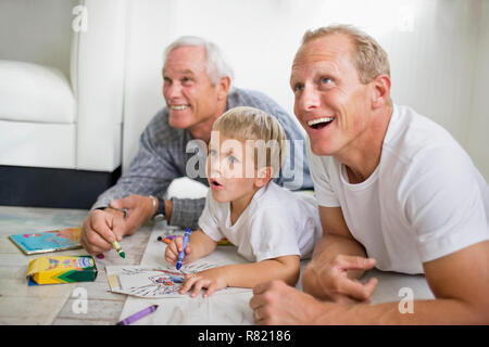 Jeune garçon avec ses mi-adultes père et grand-père d'âge mûr se trouvant sur le plancher colorier. Banque D'Images