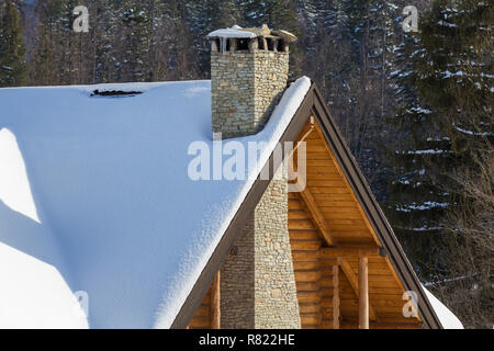 Haut de chalet traditionnel en bois de bois écologique matériaux avec pointes, haute cheminée en pierre recouvert de neige sur un grand sapin retour forêt Banque D'Images