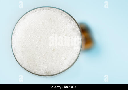 Passage près d'un verre de champagne, rempli à ras bord avec de la mousse et des bulles blanches. Cork repose sur table bleu pâle en arrière-plan flou. Banque D'Images