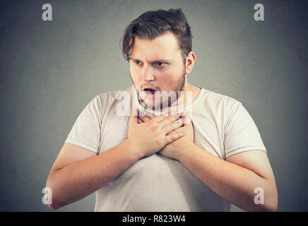 Surpoids adultes tenant la main sur la poitrine de l'homme incapable de respirer et à la recherche a souligné sur fond gris Banque D'Images