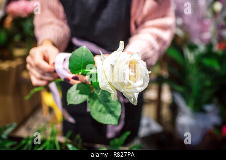 Photo d'une rose blanche dans les mains. fleuriste Stand femme et porte tablier noir. Elle est dans la salle pleine de plantes. Banque D'Images
