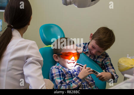 Réception à l'art dentaire. Un petit garçon se pose sur le canapé avec des lunettes, son frère qui maintiennent la lampe Banque D'Images