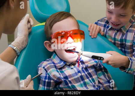 Réception à l'art dentaire. Un petit garçon est sur la table et son frère met le feu dans sa bouche Banque D'Images