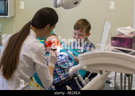 Réception à l'art dentaire. A smiling little boy jette sur la table en lunettes de protection Banque D'Images