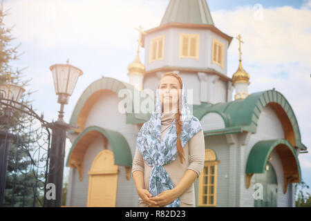 Orthodoxe russe femme d'âge moyen dans un foulard se dresse sur le fond de l'église en bois. Banque D'Images