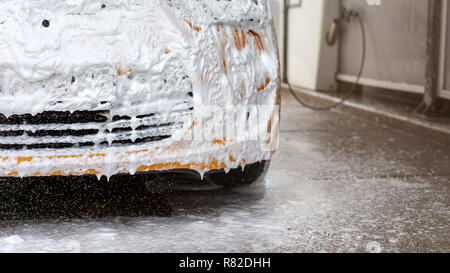 Bouclier avant de voiture jaune lavées dans carwash, complètement recouvert de mousse et de shampooing blanc, certains laissant tomber au sol. Banque D'Images