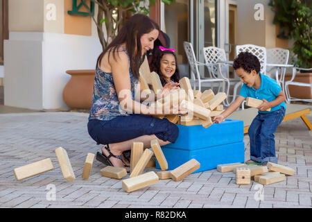 Le jumbling tower falls apart alors que tout le monde va rire et essayer de l'empêcher d'aller partout dans le patio. Maman passer du temps de qualité. Banque D'Images