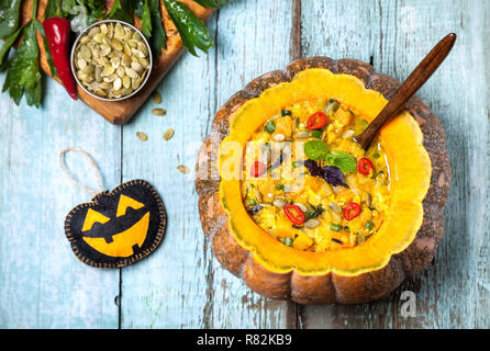 Avec la soupe de lentille dans la citrouille sculptée, semences et noir Halloween jouet sur le fond en bois bleu à Halloween party Banque D'Images