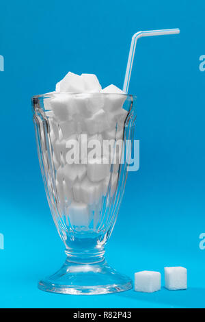 Verre de cubes de sucre à boire à la paille sur fond bleu - mauvaise alimentation concept. Banque D'Images