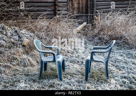 Deux chaises en plastique bleu avec blanc congelé dans un milieu rural avec jardin et maison de ferme rustique dans la glace couverte d'herbe gelée blanche un froid matin d'hiver précoce Banque D'Images