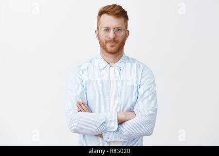 Croyez-moi, je suis professionnel. Bien déterminé à la rousse mâle-soigné dans les verres et chemise, holding hand traversé sur la poitrine dans l'auto-assurance de la posture et à la caméra, à l'écoute particulière Banque D'Images