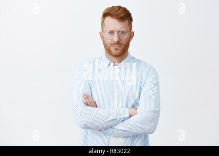 Studio shot of serious-à riche homme d'affaires en shirt et lunettes, fronçant à la caméra au strict avec calme et l'expression déterminée, traversant les mains sur la poitrine, écoutant attentivement au cours de traiter Banque D'Images