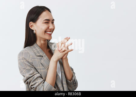 Studio shot de bonne-femme joyeuse à rire de joie et d'enthousiasme, demi-permanent mis sur fond gris, les mains jointes, à droite, se réjouissant de b-day party Banque D'Images