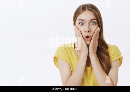 Taille plan sur impressionné sans voix bon-à la femme en jaune t-shirt holding paumes sur joues lèvres dans son pliage wow permanent déconcertés, émerveillés d'écouter les rumeurs choquantes Banque D'Images