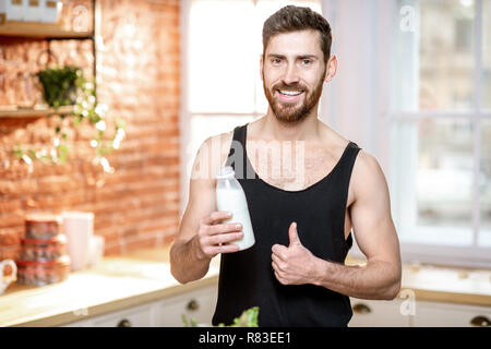 Portrait of a handsome man in black sports t-shirt boire du lait secouer sur la cuisine à la maison Banque D'Images