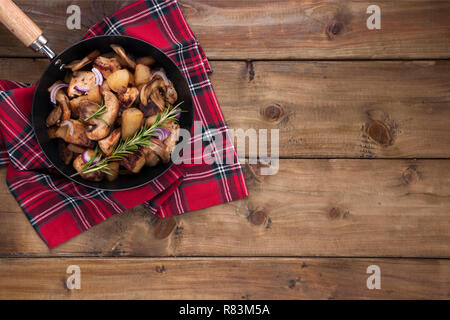 Pommes de terre sautées avec de la viande, le romarin, l'oignon et les champignons dans une casserole sur un fond de bois. Vintage photo et une serviette dans un style rustique. Espace libre pour tex Banque D'Images