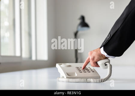 Businessman hand composer un numéro de téléphone à l'aide de téléphone fixe blanc sur blanc bureau. Banque D'Images