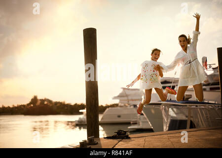 Portrait de deux sœurs rire sautant en l'air sur un quai au coucher du soleil. Banque D'Images