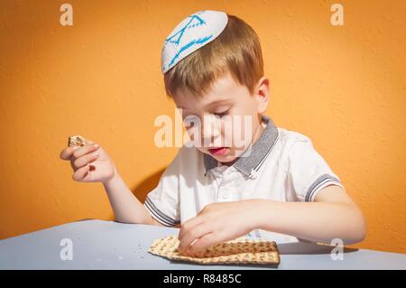 Enfant juif caucasien mignon avec une kippa sur la tête touchant le pain azyme traditionnelle. Pâque juive Pessah notion de droit. Banque D'Images